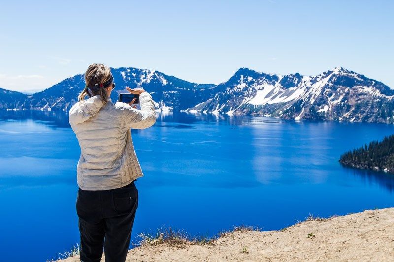 woman taking photo of Crater Lake