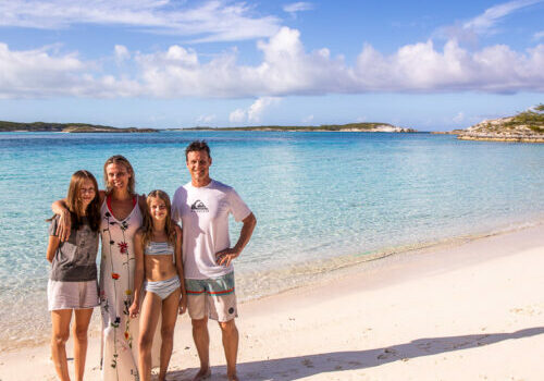Family of four getting a phot taken on the beach with beautiful blue water behind them
